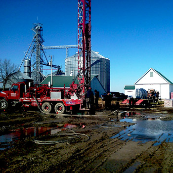 Colored photo of red rotary drilling rig at agricultural site 